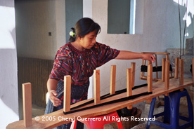 Preparing the warp for a huipil on a warping board is the first step of weaving on a back strap loom.  The same board can be used for preparing the warp for shawls and headcloths.  Photo by Cheryl Guerrero 2005.