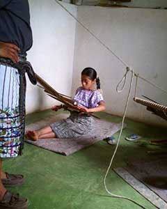 Antonia Quevac, 10, proudly weaves for the Cojolya Association in Santiago Atitlán when she is not in school.  The association has a museum and sales area, and exports to the U.S. and abroad.  Antonio Ramirez, a guide for the group, stands to the left, wearing the traditional traje of indigenous men from the area.  Photo by Paul G. Vitale 2005.